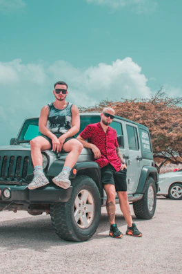 two men sitting on the back of a green jeep