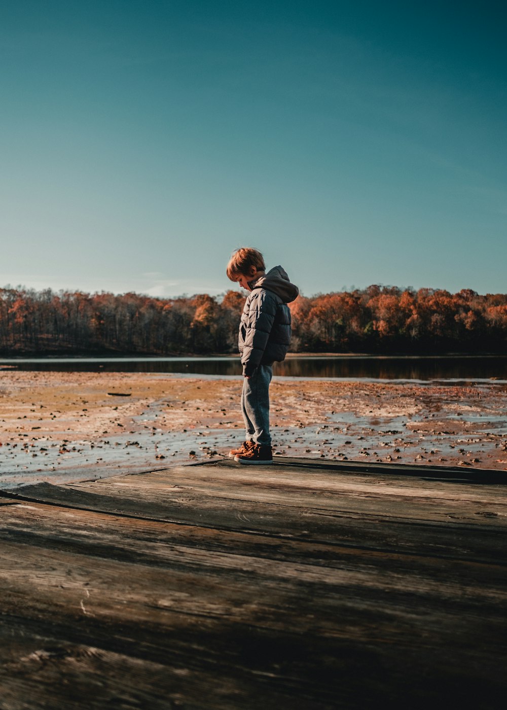 a boy standing on a dock looking at the water