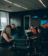 a group of people sitting around a table with laptops