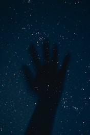 a person's hand is silhouetted against the night sky