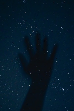 a person's hand is silhouetted against the night sky