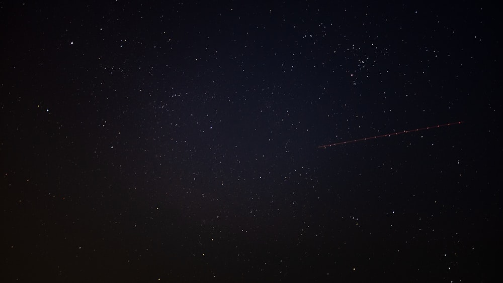 a night sky with stars and a plane in the distance