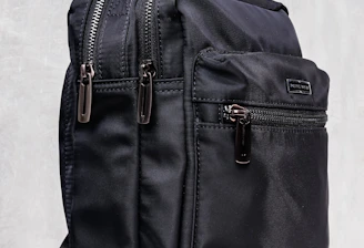 A sleek black backpack with multiple zippered compartments and a sturdy carrying handle. The design is minimalist and practical, suggesting functionality and durability.