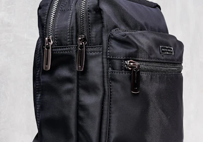 A sleek black backpack with multiple zippered compartments and a sturdy carrying handle. The design is minimalist and practical, suggesting functionality and durability.