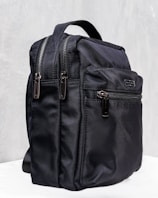 A sleek black backpack with multiple zippered compartments and a sturdy carrying handle. The design is minimalist and practical, suggesting functionality and durability.