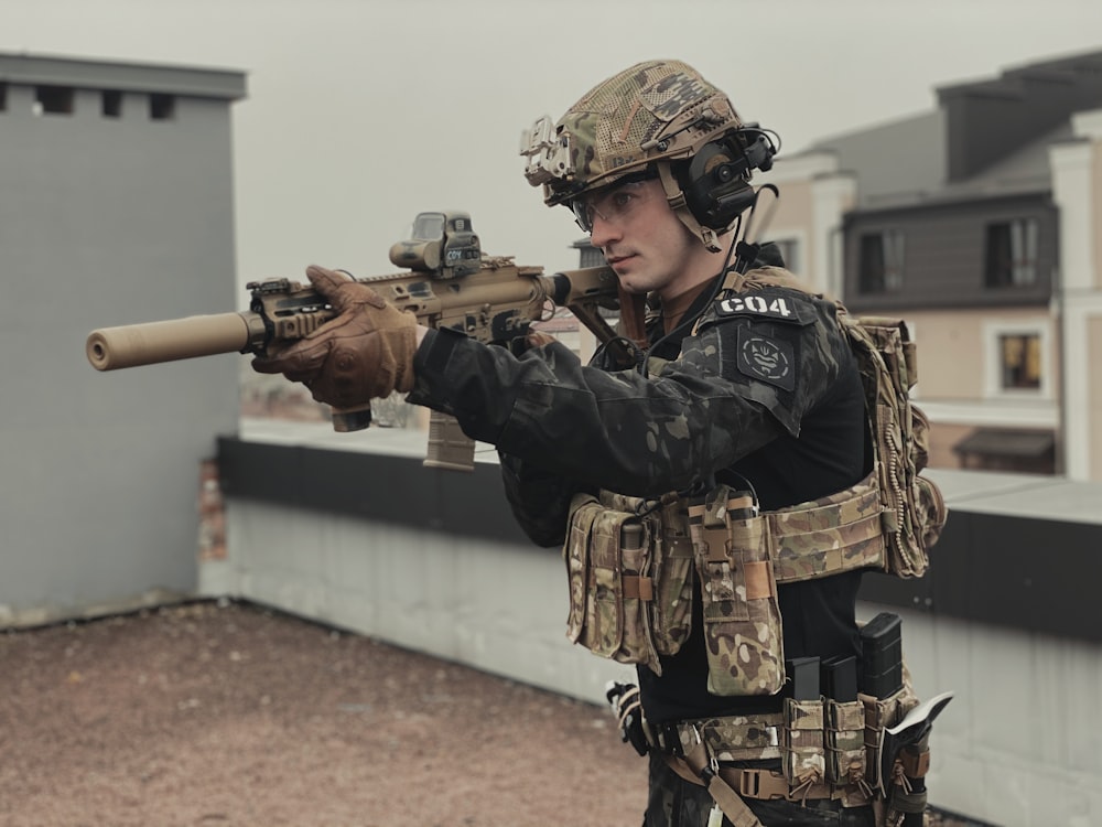 a man in camouflage holding a rifle on a roof