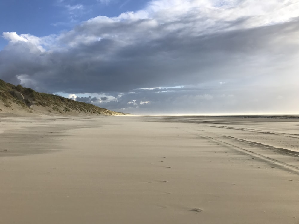 a sandy beach under a cloudy sky with footprints in the sand