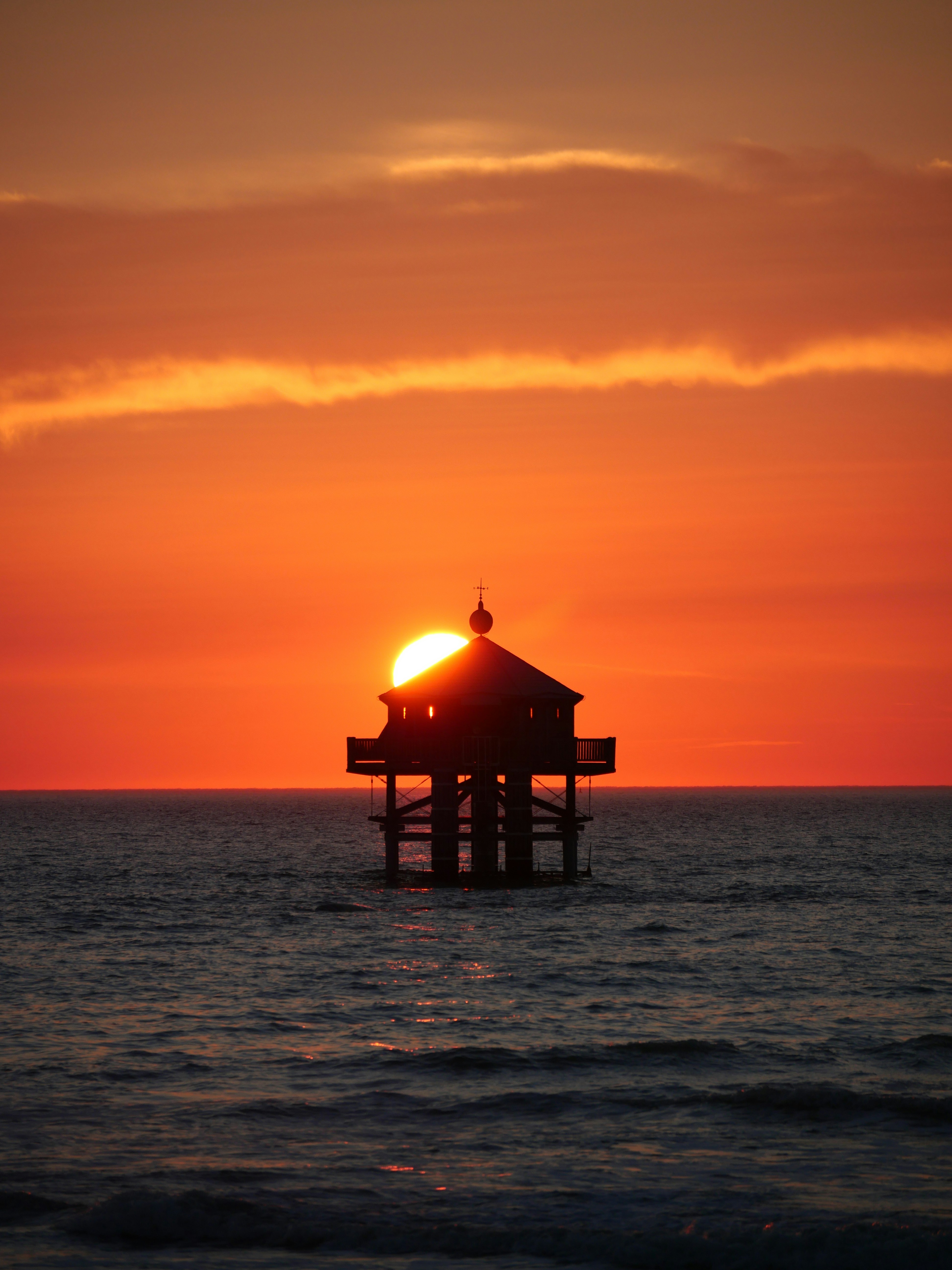 the sun is setting over the ocean with a pier in the foreground