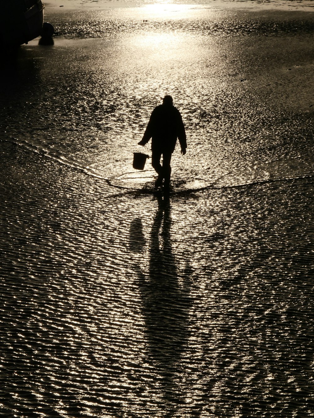a man walking across a wet beach holding a bucket