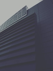 A modern building with a geometric design, featuring dark horizontal slats and a grid-like window structure. The architectural style conveys a sense of minimalism and sleekness.