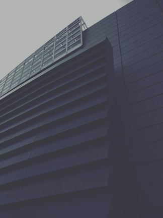 A modern building with a geometric design, featuring dark horizontal slats and a grid-like window structure. The architectural style conveys a sense of minimalism and sleekness.