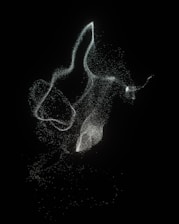 A collection of swirling, luminous particles forms ethereal shapes against a dark background. The particles are scattered loosely, creating a sense of movement and fluidity.