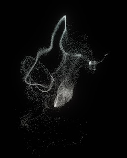 A collection of swirling, luminous particles forms ethereal shapes against a dark background. The particles are scattered loosely, creating a sense of movement and fluidity.