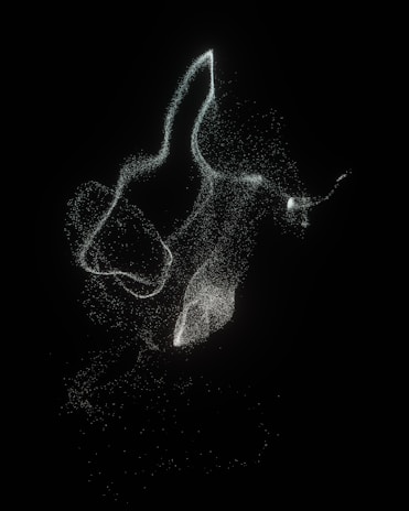 A collection of swirling, luminous particles forms ethereal shapes against a dark background. The particles are scattered loosely, creating a sense of movement and fluidity.