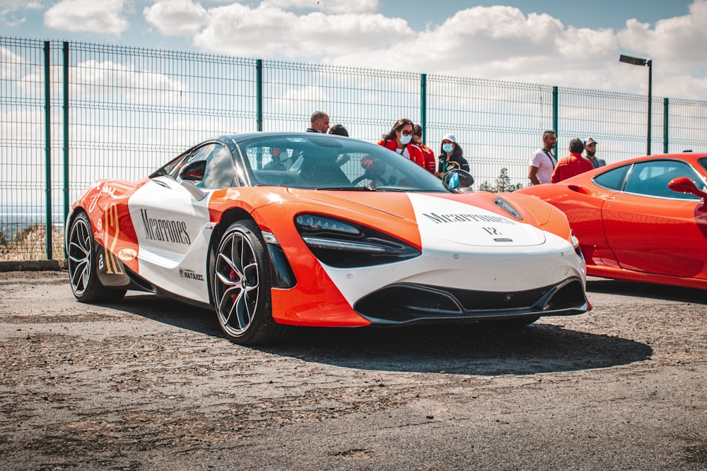 a white and orange sports car parked in front of a fence