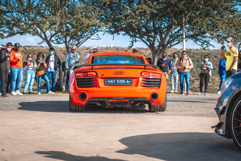 an orange sports car parked in front of a group of people