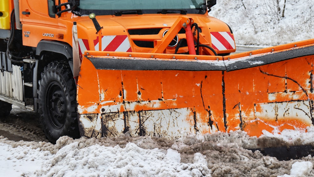 a large orange truck driving down a snow covered road