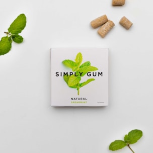A package of Simply Gum with a spearmint leaf illustration centered on a white background. The package is accompanied by mint leaves and several brownish gum pieces nearby, creating a natural and fresh aesthetic.