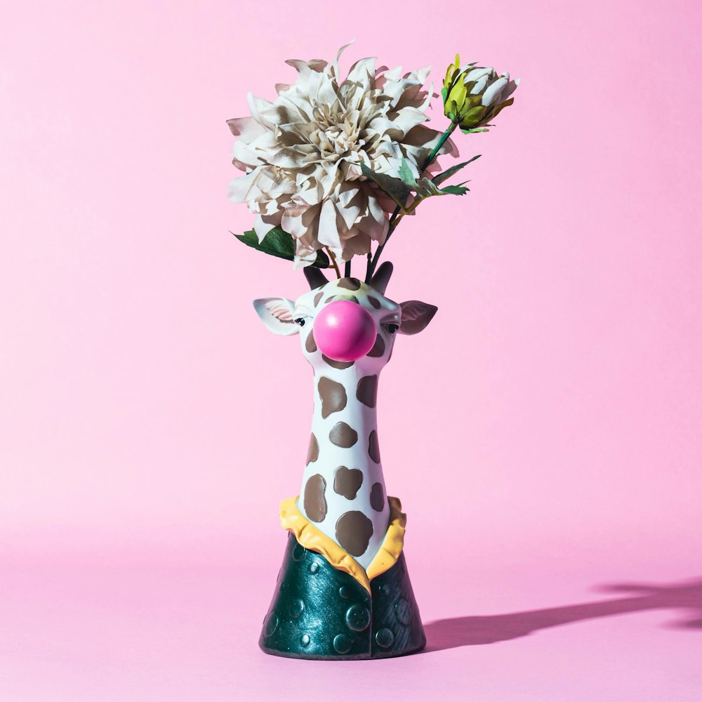 a giraffe vase with flowers in it on a pink background