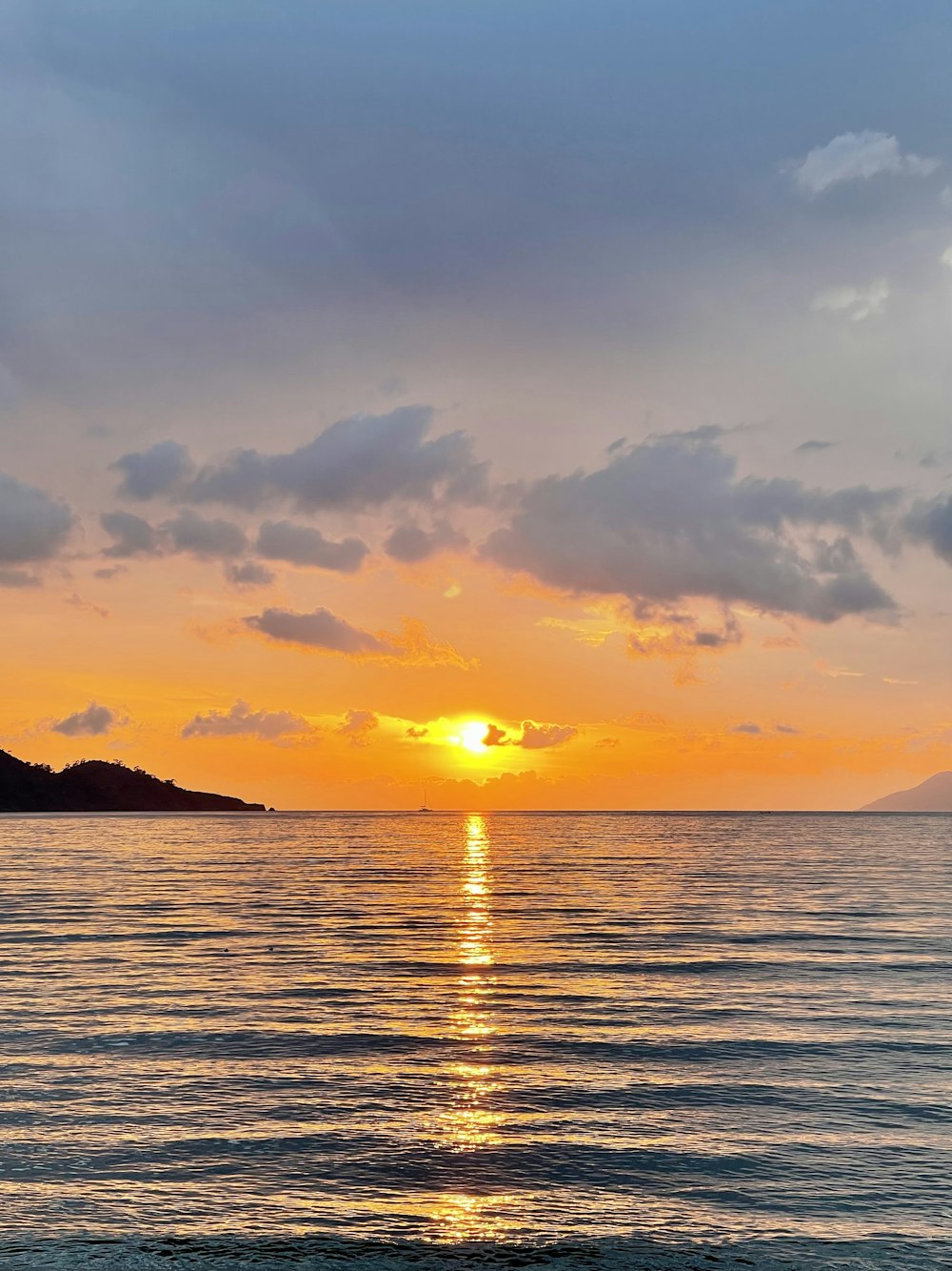 o sol está se pondo sobre o oceano com uma pequena ilha à distância