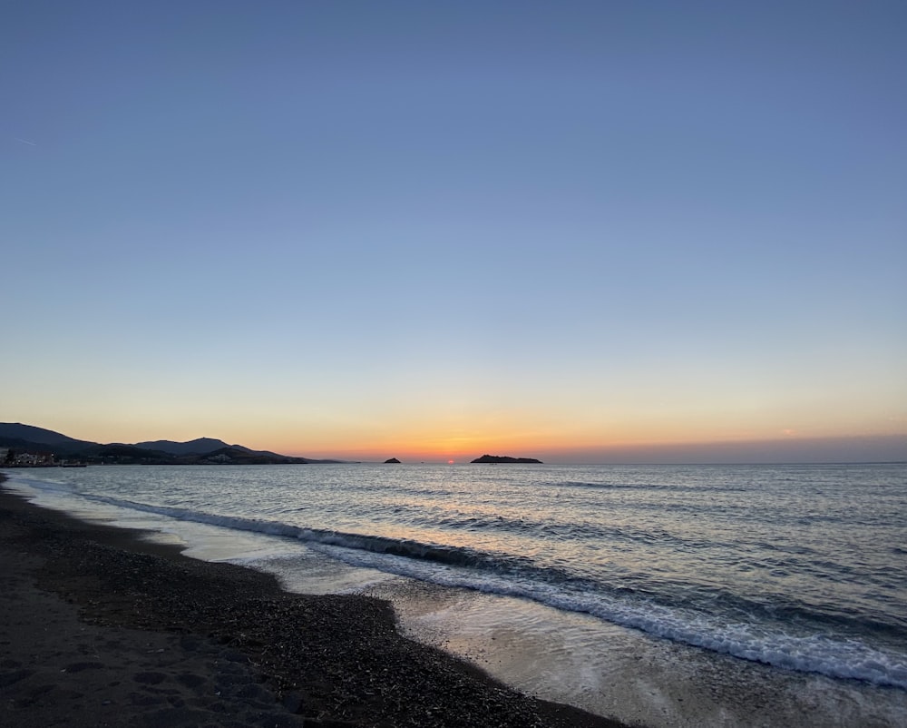 the sun is setting over the ocean on the beach