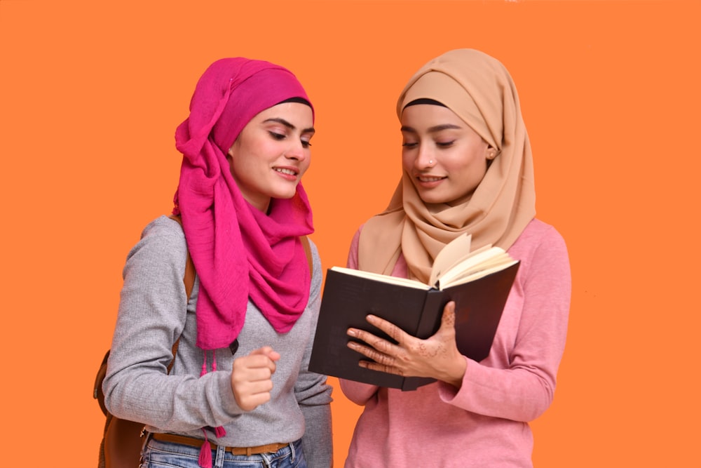 two women in hijabs are reading a book