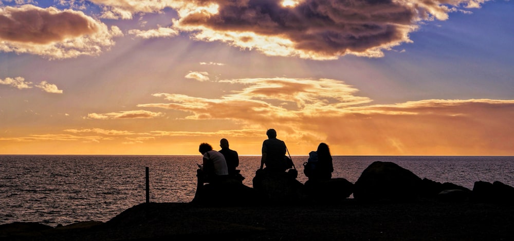 a group of people sitting on top of a rock near the ocean