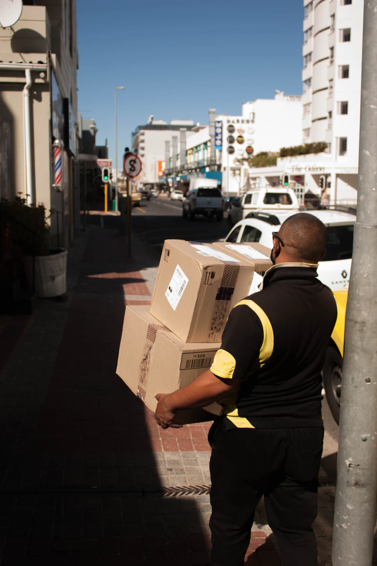 A courier carrying a parcel along a city street toward the final handoff of a delivery run