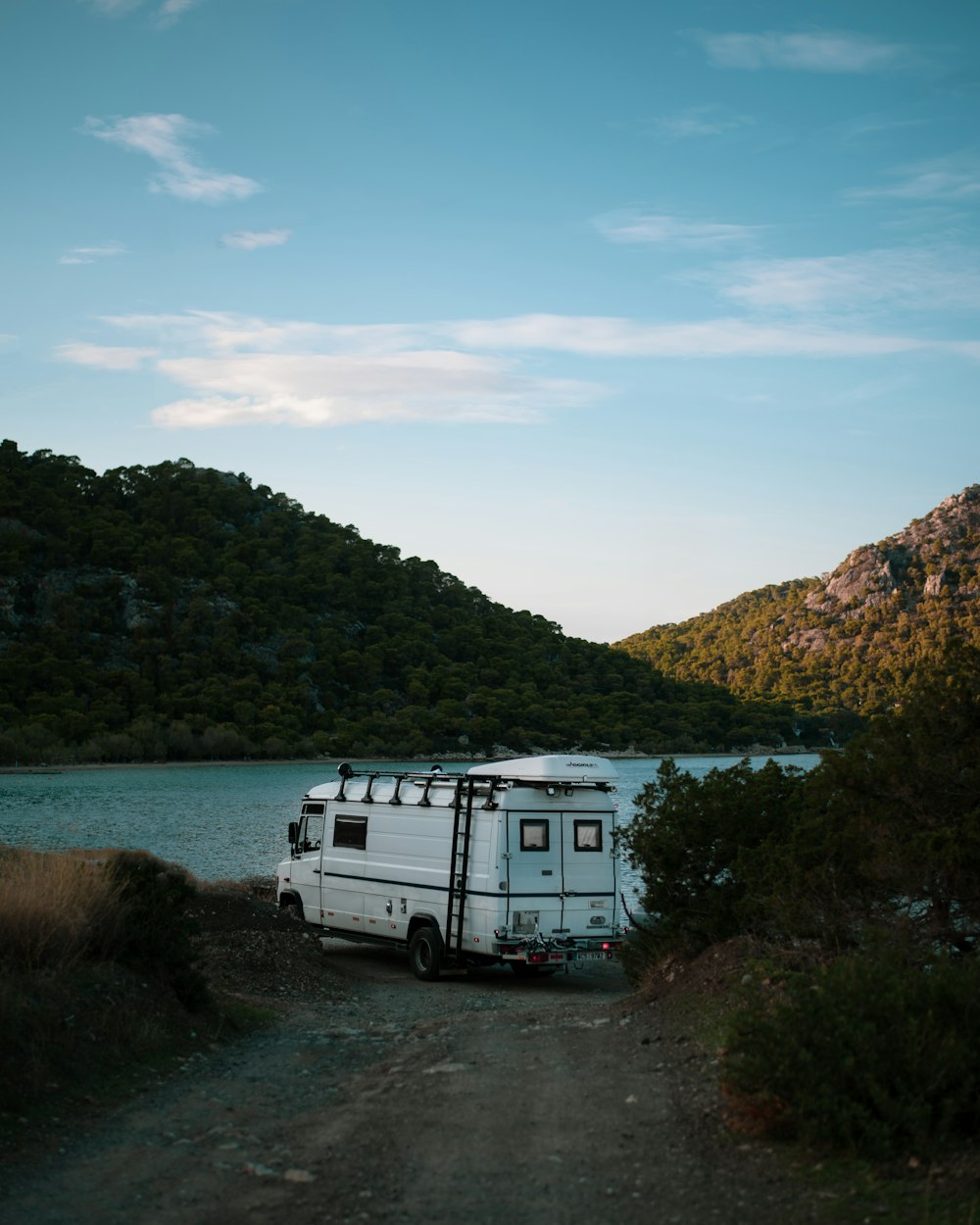 a camper van parked on a dirt road next to a body of water