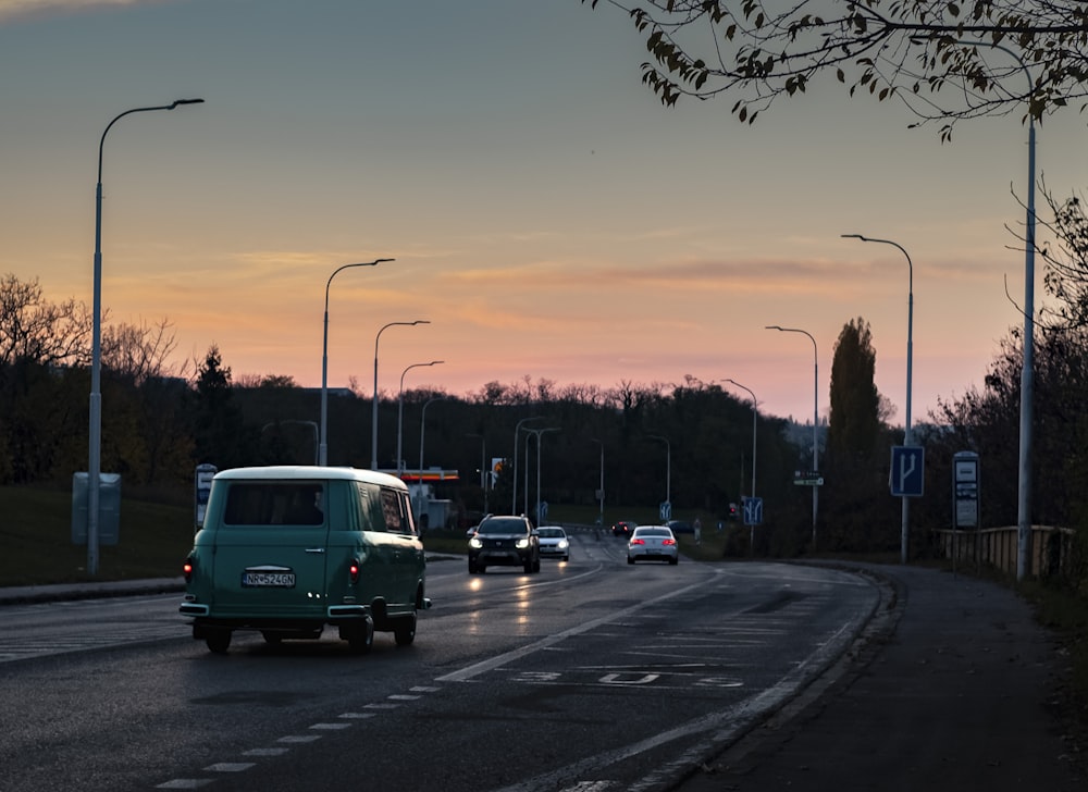 a green van driving down a street next to a forest