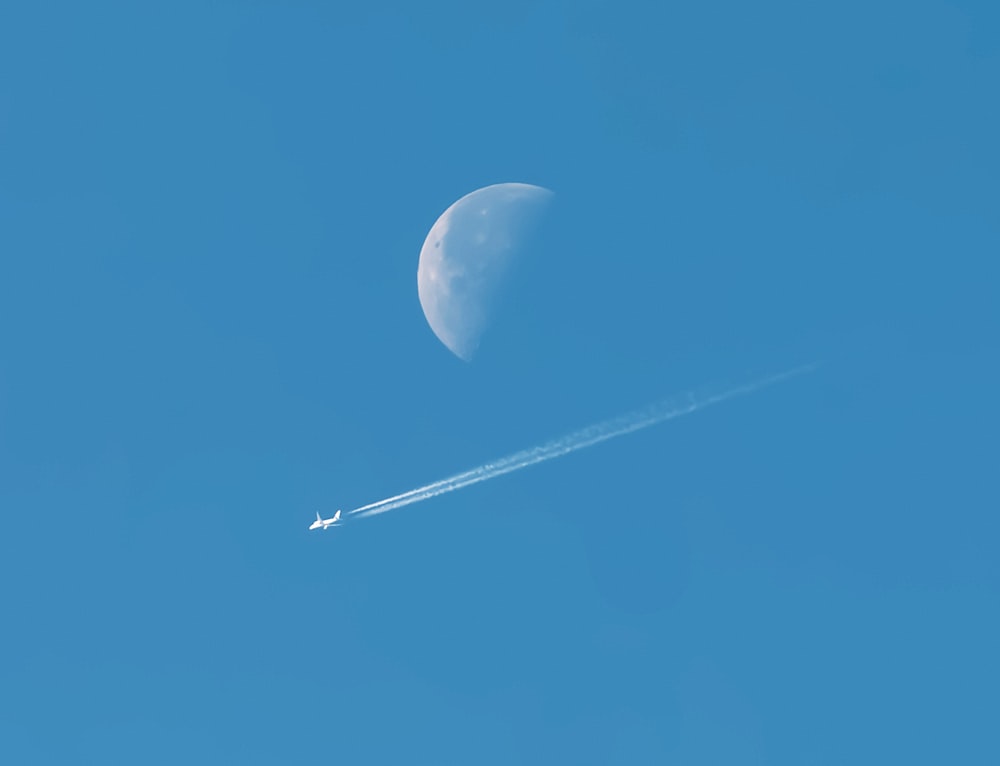 a plane flying in the sky with a half moon in the background