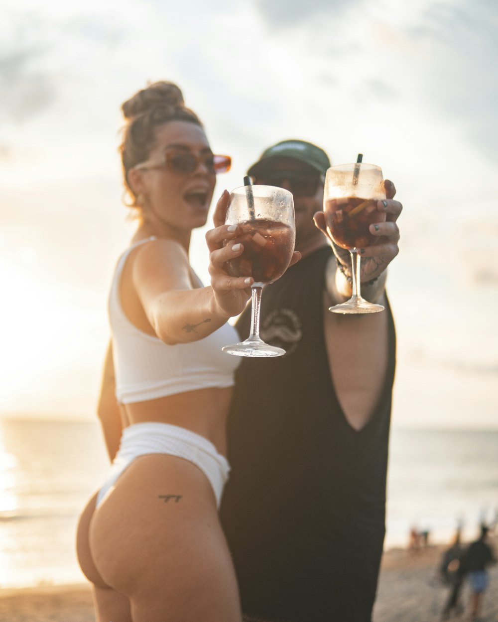 a man and a woman standing on a beach holding wine glasses