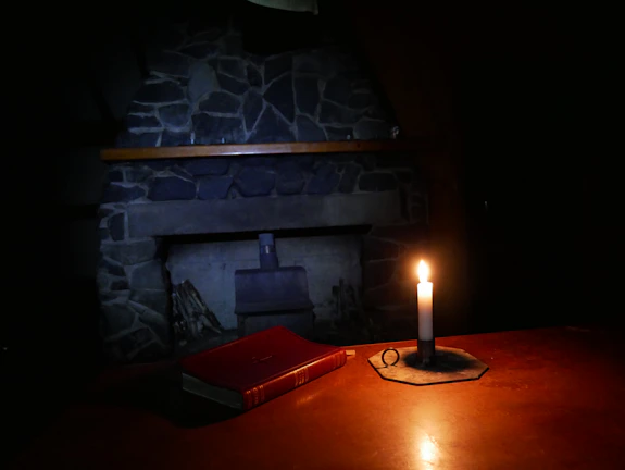 A dimly lit room with a flickering candle casting shadows on a mysterious old book.