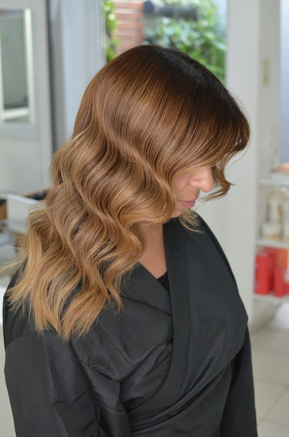 Colourist in black gloves applying lightener to a section of hair with a tint brush.