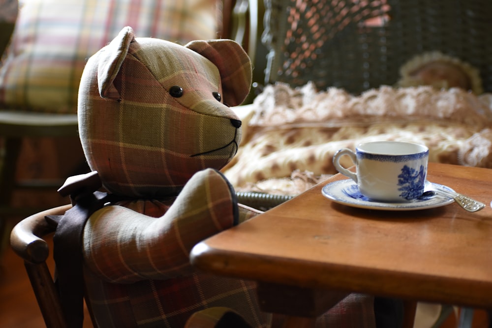 a teddy bear sitting at a table with a cup and saucer