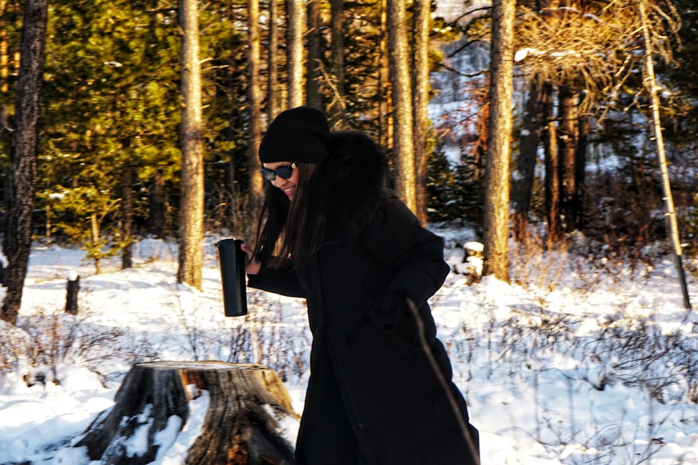 a woman standing in the snow next to a tree stump