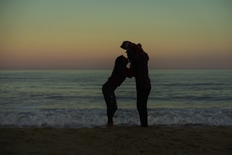 a couple of people standing on top of a sandy beach