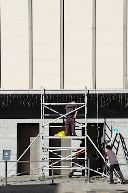A skilled worker assembling scaffolding on a sunny day in a coastal Italian town.