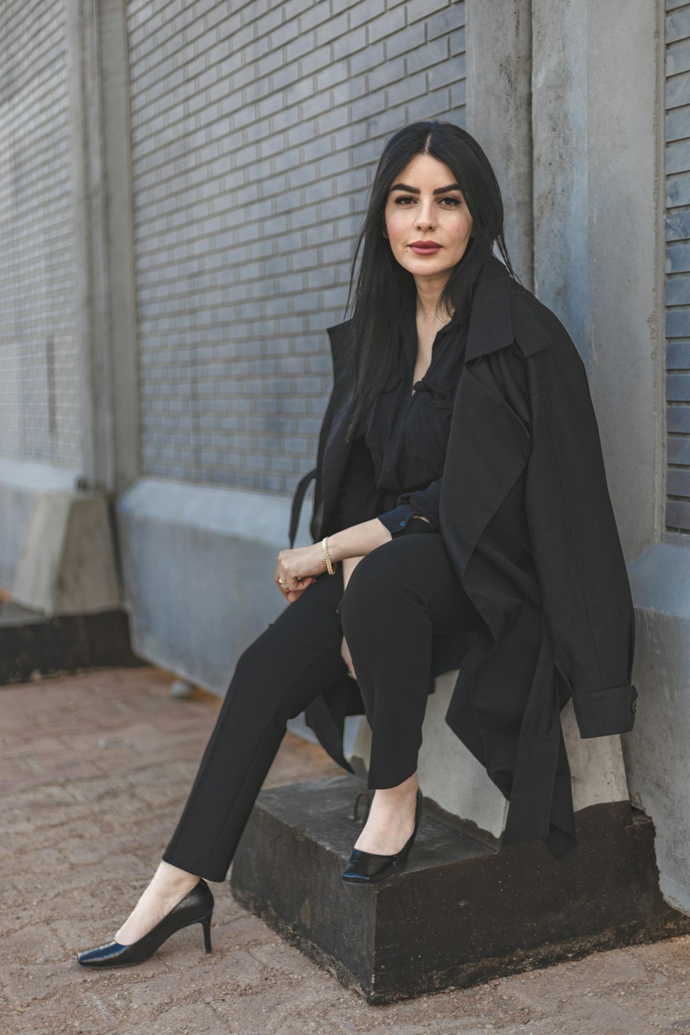 a woman sitting on top of a bench next to a brick wall