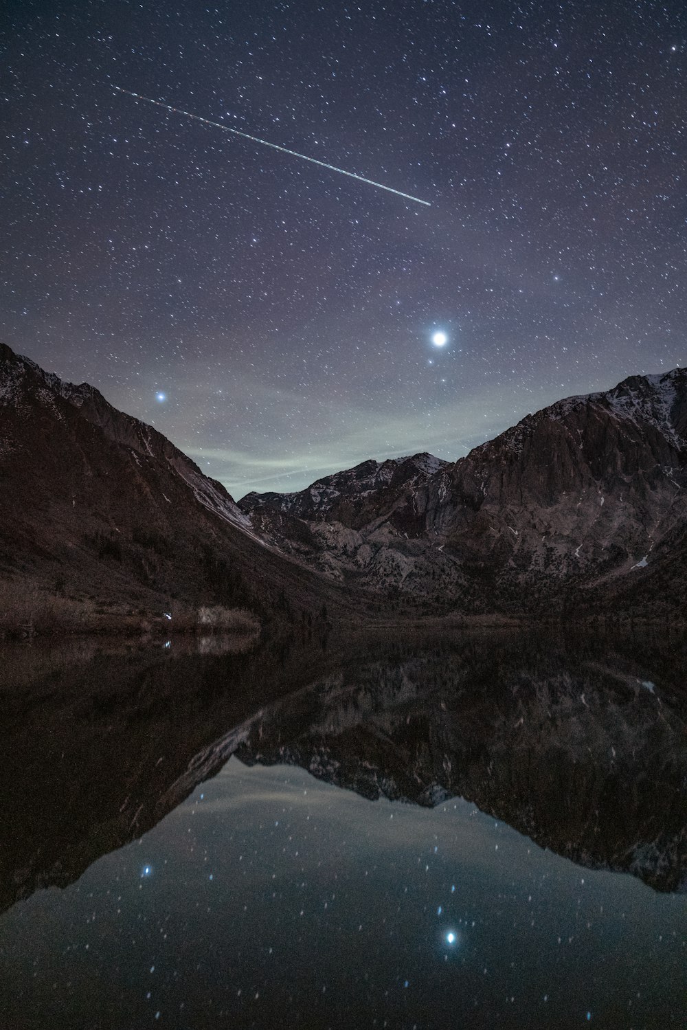 the night sky is reflected in the still water of a mountain lake