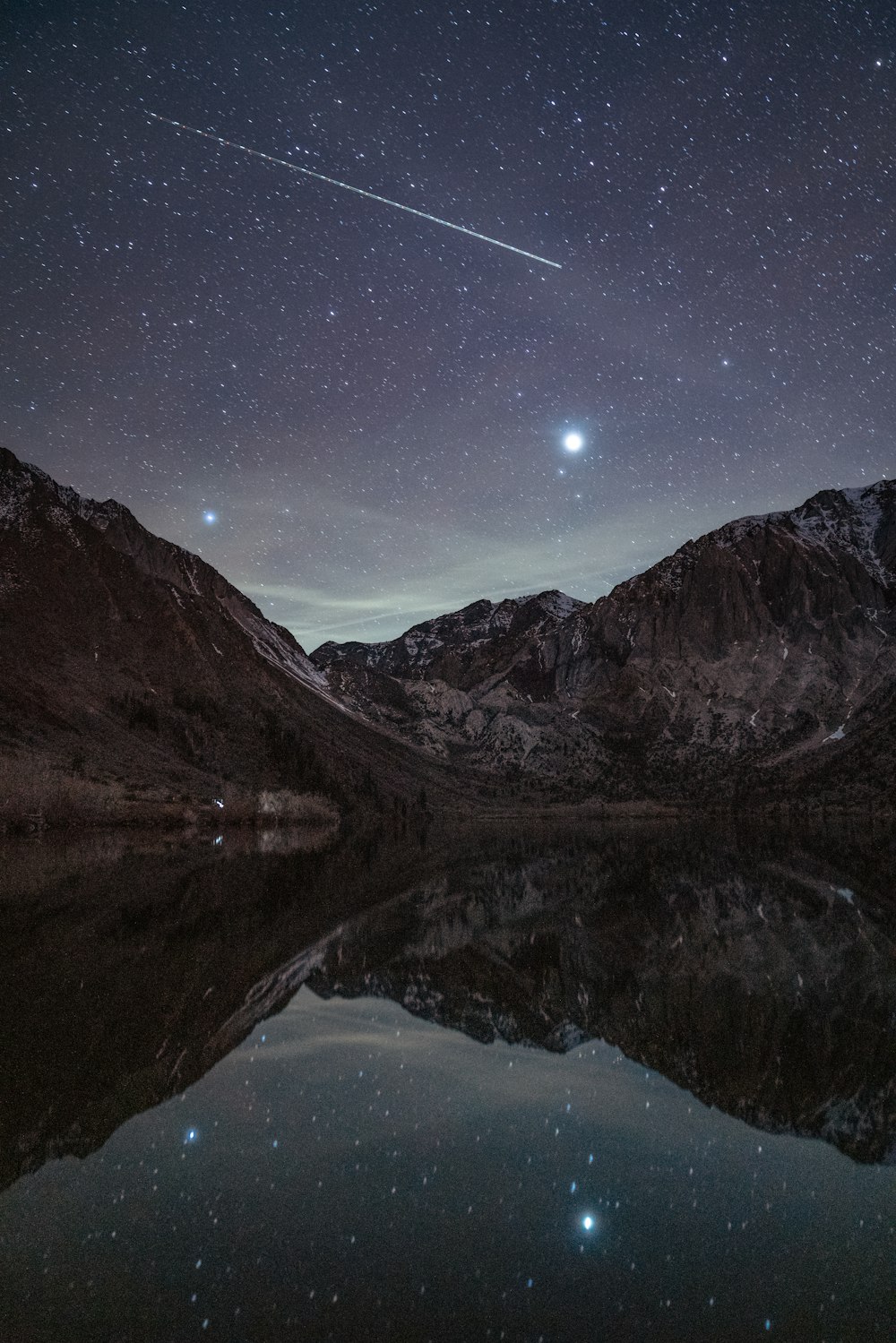 Il cielo notturno si riflette nell'acqua ferma di un lago di montagna