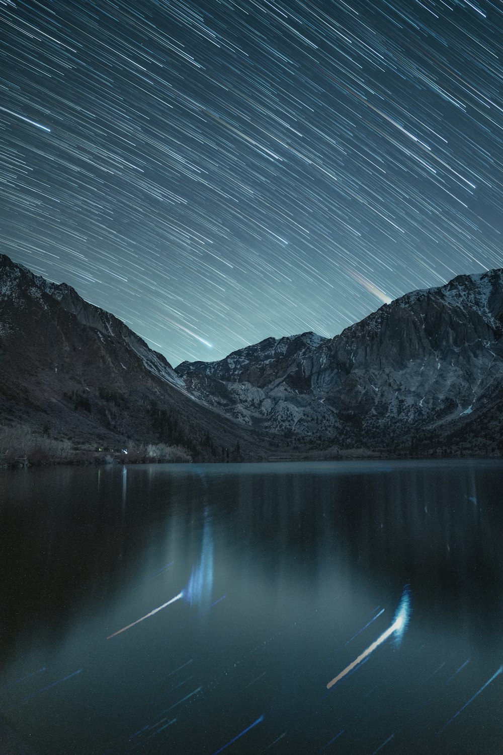 the night sky is lit up over a mountain lake