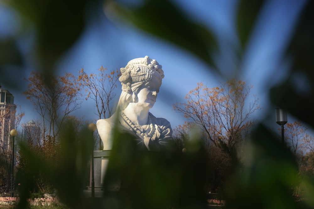 a statue of a woman is seen through the leaves of a tree