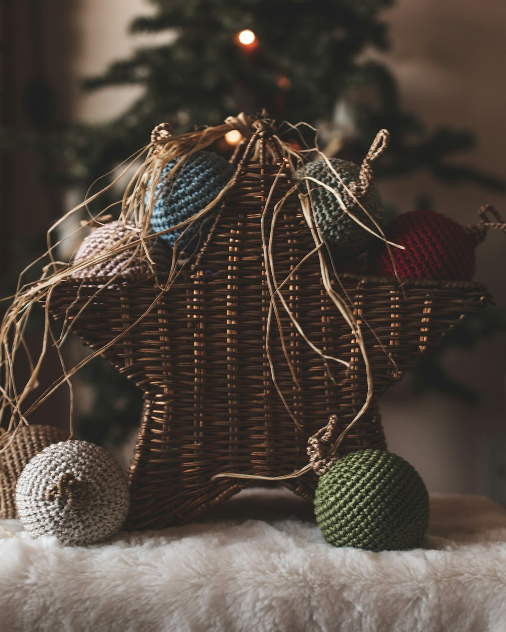 a wicker basket with balls of yarn in front of a christmas tree