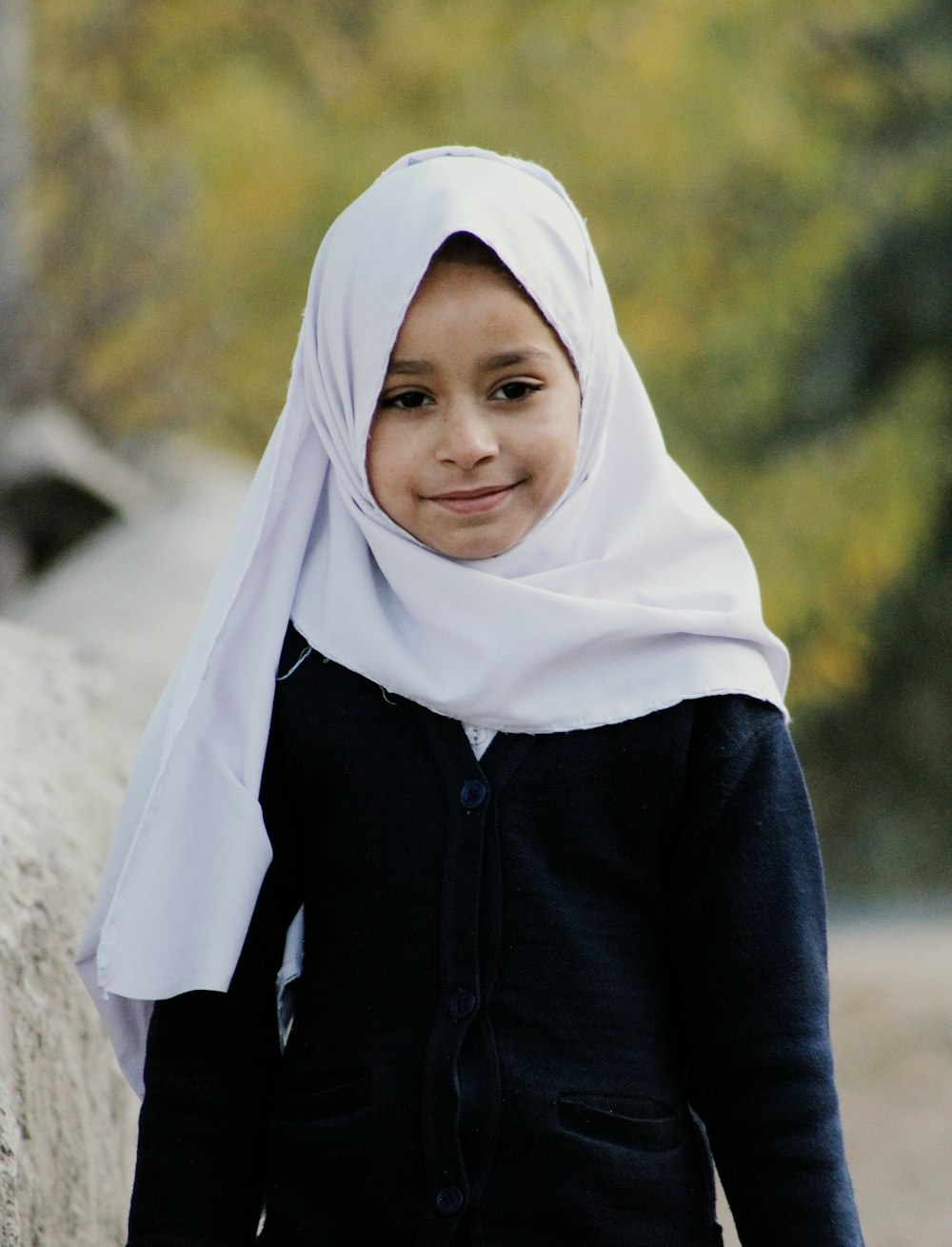 a young girl wearing a white headscarf standing next to a stone wall