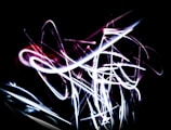 A series of dynamic, neon light trails in white and pink against a dark background, creating an abstract and energetic pattern.