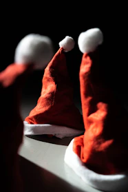 A festive display of classic red Christmas hats arranged on a wooden table with twinkling lights in the background.