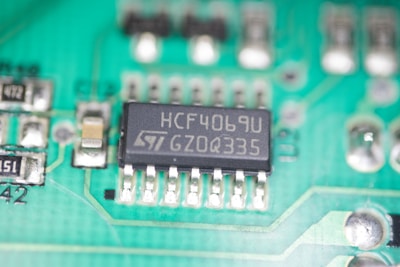 A close-up view of a green printed circuit board featuring an integrated circuit chip marked with the text 'HCF4069U GZ0Q335'. The board also contains various small electronic components such as resistors and capacitors, and conductive traces that form connections between components.