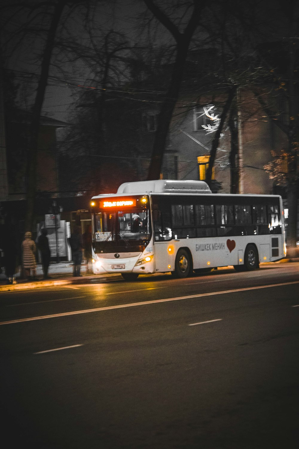 a white bus driving down a street at night