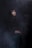 A person wearing a dark cloak is gazing upwards surrounded by a smoky, atmospheric background. Their hands are folded and resting on their lap, and the lighting creates an ethereal and mysterious ambiance.
